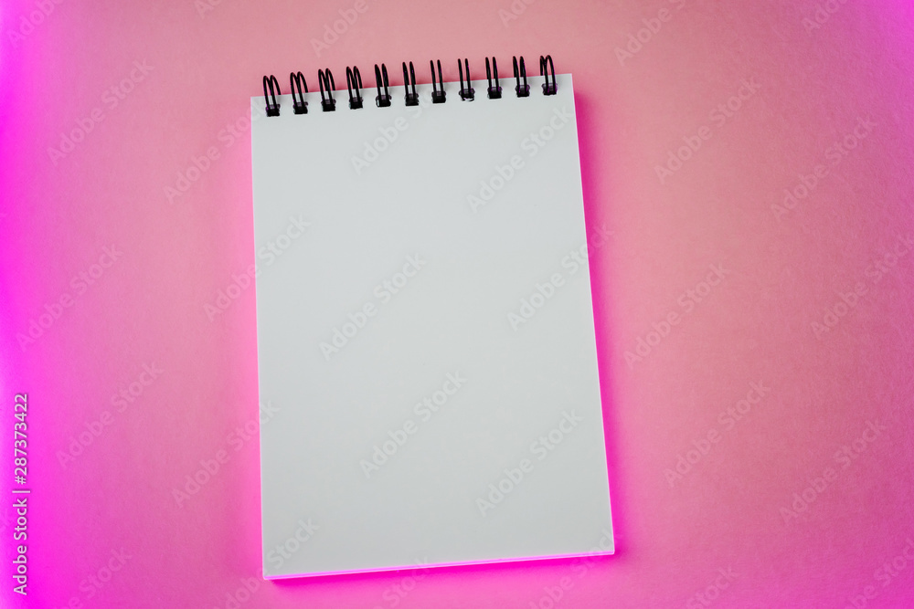 An open white notebook on a spiral lies on a pink paper background with a neon stylish trend highlight. Place for text. Concept of ideas, notes. Minimalism, flat lay, top view. An open white notebook on a spiral lies on a pink paper background with a neon stylish trend highlight. Place for text. Concept of ideas, notes. Minimalism, flat lay, top view.