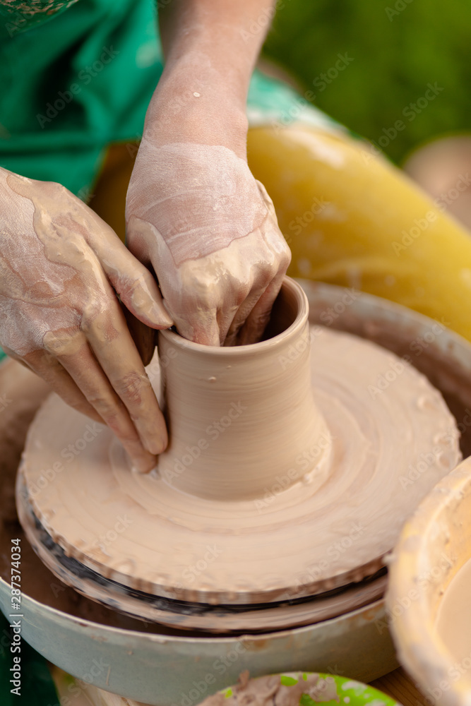 Hand craft making pottery on wheel. Female hands mold ceramic plate from clay (pot).