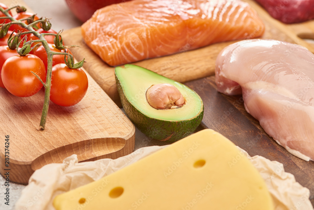 Fresh raw fish, poultry, cheese, branch of cherry tomatoes and half of avocado on wooden cutting boards Fresh raw fish, poultry, cheese, branch of cherry tomatoes and half of avocado on wooden cutting boards