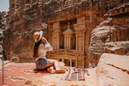 Young woman tourist sitting on a cliff after reaching the top, Al Khazneh in the ancient city of Petra, Jordan, UNESCO World Heritage Site photo