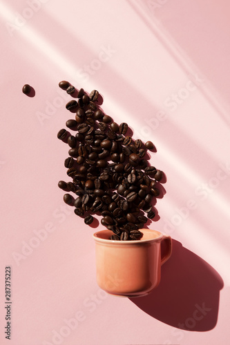 Coral colored cup with effuse coffee's beans with shadows on pastel rose background. Flat lay. Top view. Coffee concept. Pop art still life photo