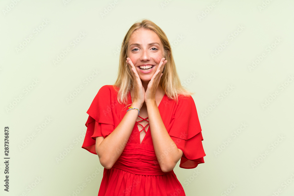 Blonde young woman over isolated green background with surprise facial expression Blonde young woman over isolated green background with surprise facial expression