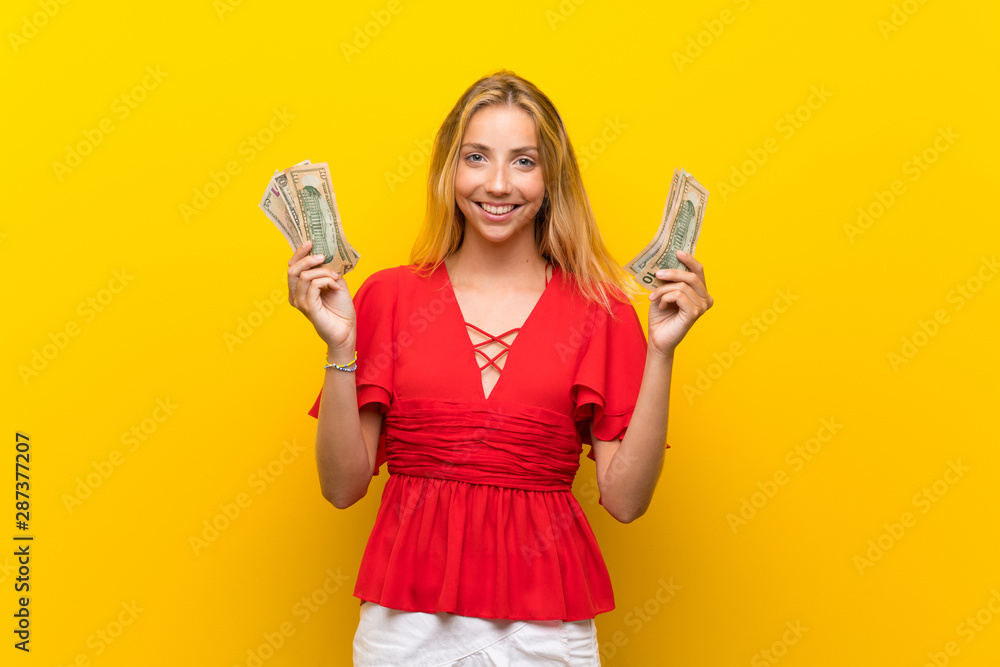 Blonde young woman over isolated yellow background taking a lot of money Blonde young woman over isolated yellow background taking a lot of money