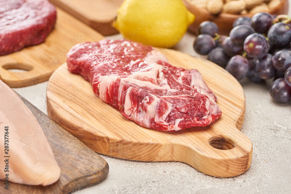 Raw mmeat tenderloin on wooden cutting board near grapes and lemon on marble surface