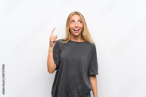 Blonde young woman over isolated white background pointing up and surprised