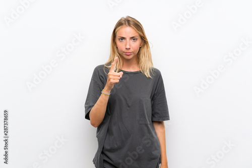 Blonde young woman over isolated white background frustrated and pointing to the front