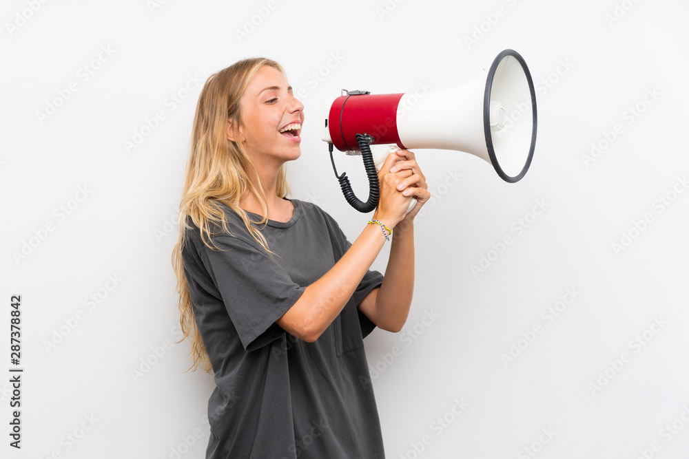 Blonde young woman over isolated white background shouting through a megaphone Blonde young woman over isolated white background shouting through a megaphone