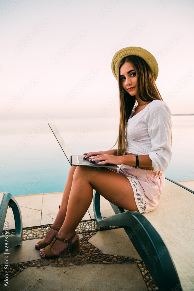 Young beautiful woman working on laptop in a swimming pool