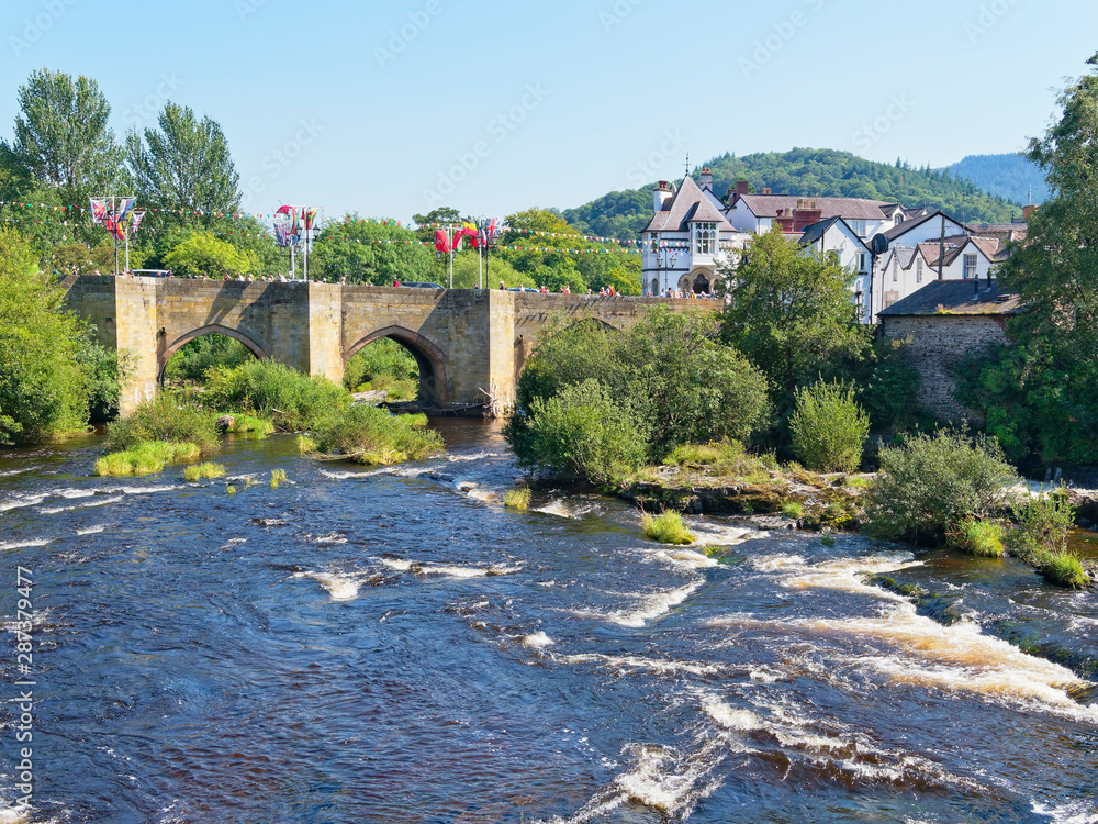 The River Dee flows quickly under the old arched stone bridge in Llangollen, Cymru.