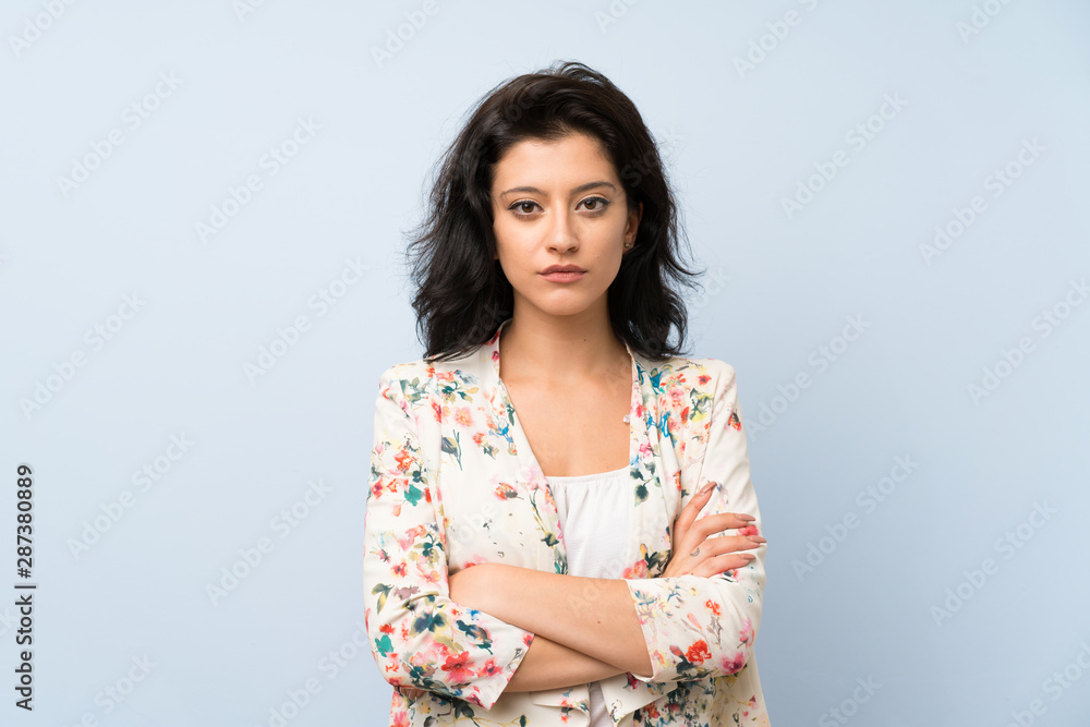 Young woman over isolated blue background keeping arms crossed Young woman over isolated blue background keeping arms crossed