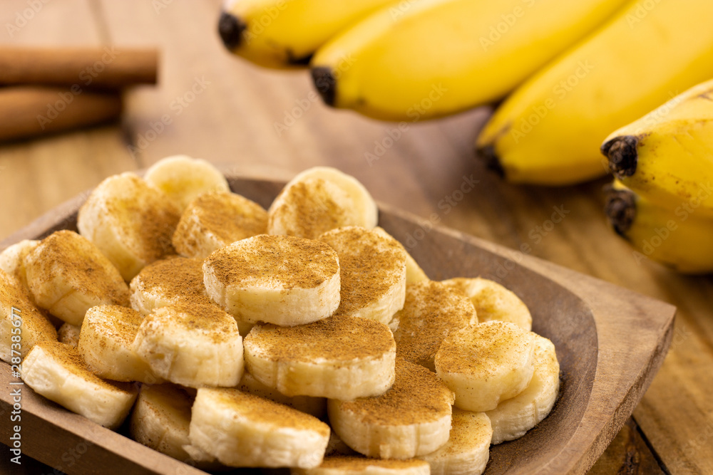 banana slices with cinnamon sprinkled and cinnamon sticks with bunch of bananas in the background banana slices with cinnamon sprinkled and cinnamon sticks with bunch of bananas in the background