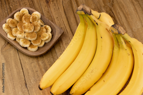 bunch of ripe bananas on wooden table with banana slices with cinnamon sprinkled on top in rustic pot