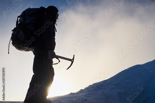 Silhouette of alpinist man going to the top of mountain at sunrise. Holding an ice tool in his hands