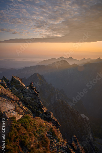 Man hiker sitting on the peak of mountain looking on sunrise