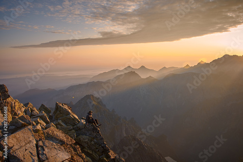 Man hiker sitting on the peak of mountain looking on sunrise