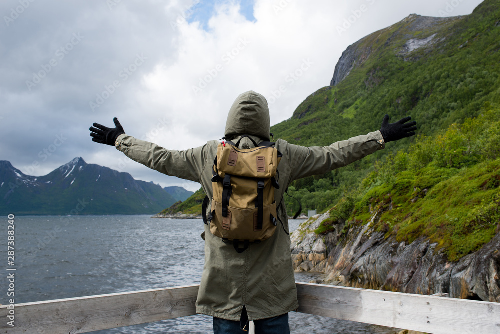 A man in a jacket and backpack enjoys the beauty of the fjord in Norway. Beautiful nature landscape in North. Amazing scenic outdoors view. Travel, adventure, lifestyle. Lofoten Islands. Scandinavia