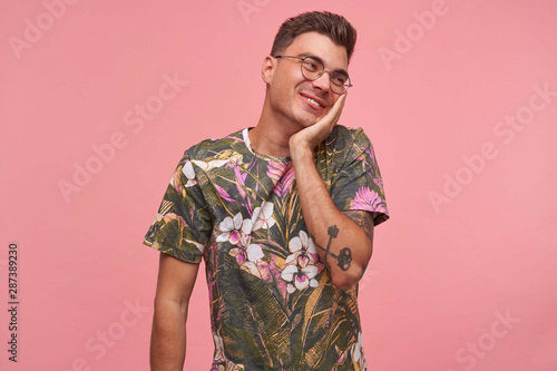 Papier peint Indoor portrait of cute shy young guy with palm on his cheek, wearing glasses an