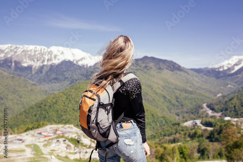 Rear view of an independent slim athletic young girl athlete in good physical shape admires the gorgeous view of the mountains and valley on a sunny summer day. Concept of new discoveries and extreme