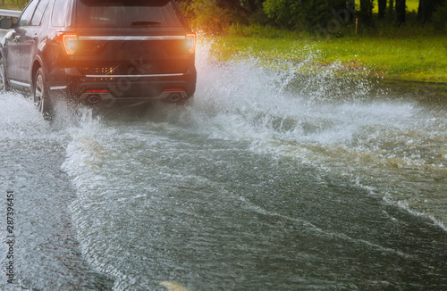 Obraz na plátně Spraying water of a car moving driving car on flooded road during flood caused by torrential rains