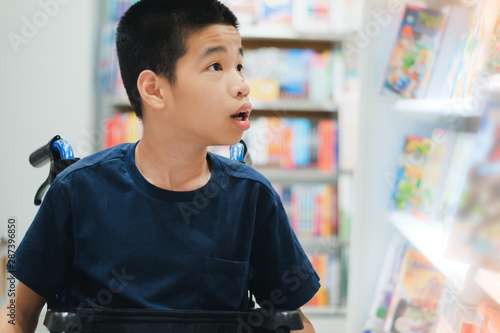 Disabled child on wheelchair is choosing books from shelves in school library, Special children's lifestyle, Life in the education age of disabled children, Happy disability kid concept.