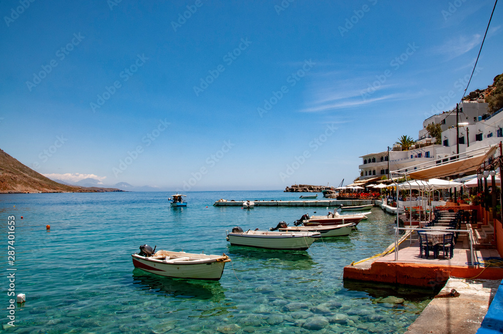 Small boats in the harbour of Loutro on Crete with torquoise waters and traditional buildings and restaurants