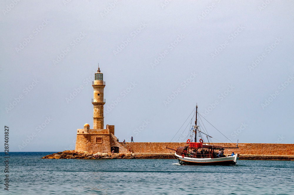 Boat leaving the harour of Chania, Crete with the unrecognizable people on the  harbour wall by the lighthouse