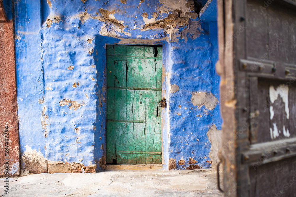 Close-up view of an old blue house with a green wooden door in Jodhpur, Rajasthan, India. Jodhpur is the second-largest city in the Indian state of Rajasthan, India. Close-up view of an old blue house with a green wooden door in Jodhpur, Rajasthan, India. Jodhpur is the second-largest city in the Indian state of Rajasthan, India.