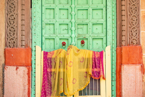 Obraz na płótnie Stunning view of a traditional Indian home with a green wooden door and colorful traditional Indian clothes (Sari) hanging to dry. Blue City of Jodhpur, Rajasthan, India. w salonie