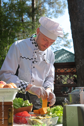 A cook in special clothes in the park prepares snacks for the holiday. The concept of servicing holidays and corporate parties. Field service.