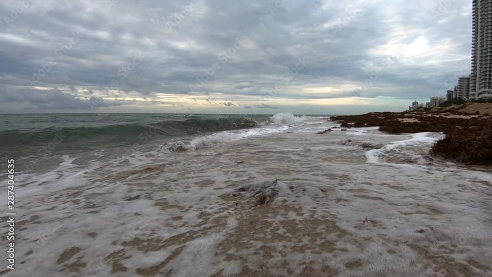 Slow motion low angle forward moving view Atlantic ocean water waves hitting fine sand shore on dramatic sunrise, Miami Beach Slow motion low angle forward moving view Atlantic ocean water waves hitting fine sand shore on dramatic sunrise, Miami Beach