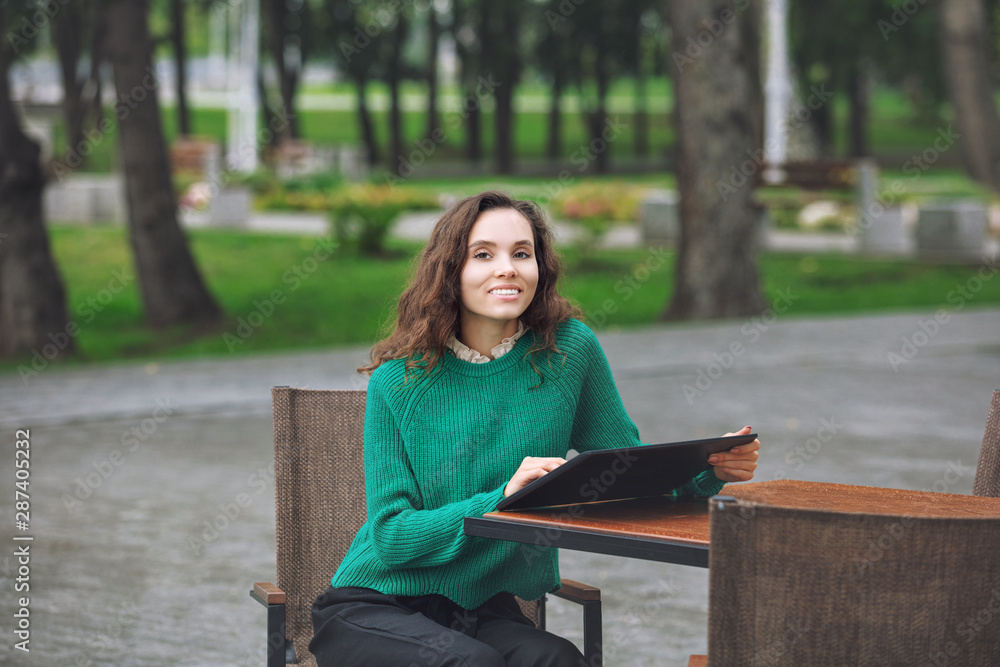 Obraz premium Young beautiful adult girl with natural makeup fashionable and happy with tablet in summer cafe