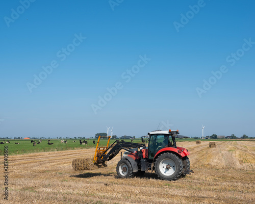 farmer with tractor collects straw bales on sunny summer day in dutch province of groningen