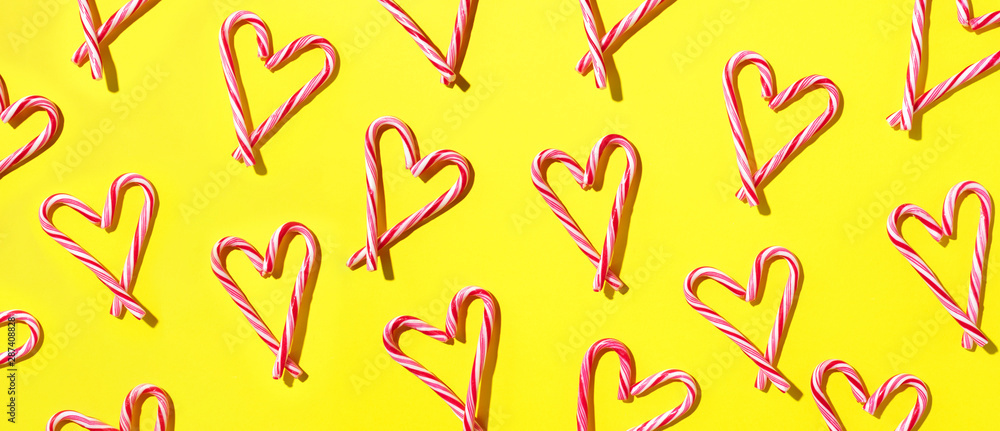 Pattern with hearts made of Christmas candy canes on yellow background. Top view. Flat lay. Love, Valentines day concept. New year and Christmas card Pattern with hearts made of Christmas candy canes on yellow background. Top view. Flat lay. Love, Valentines day concept. New year and Christmas card