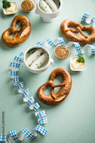 Münchener Weißwurst in Terrine mit bayrischer süßen Senf, Brezel und Butter mit Oktoberfest Luftschlangen auf Pastell grünen Hintergrund photo