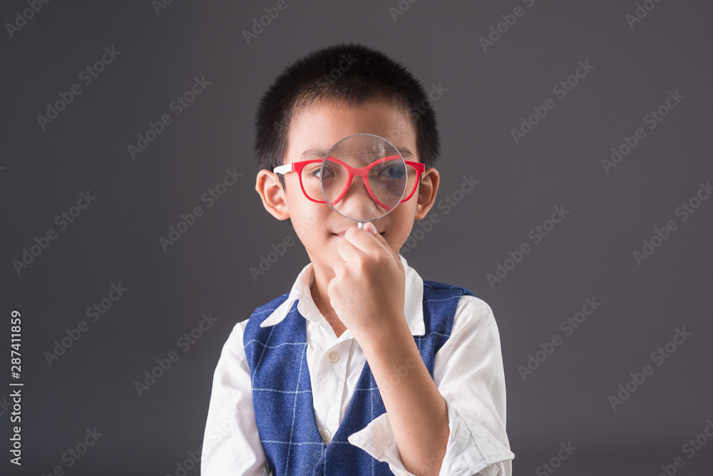 Genius boy in suit on gray background, Asian boy wearing glasses and holding a Magnifying glass in hand,kid and education concept Genius boy in suit on gray background, Asian boy wearing glasses and holding a Magnifying glass in hand,kid and education concept