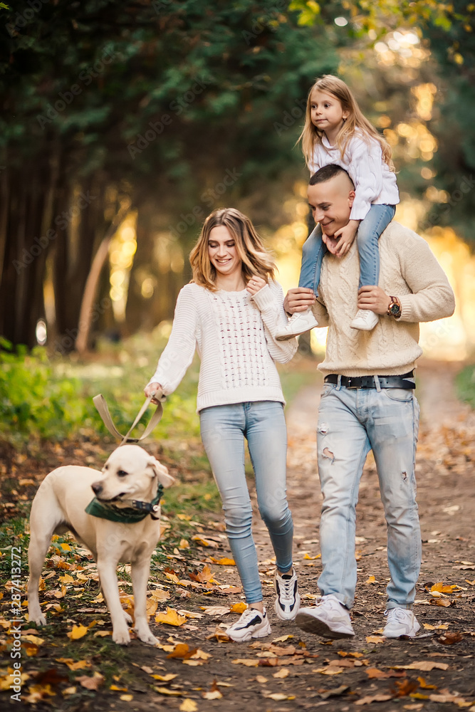 Obraz premium Happy beautiful family with dog labrador is having fun together walking the in park.