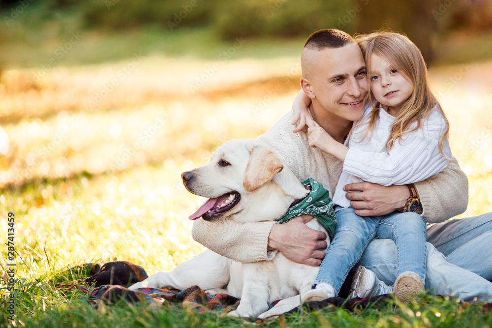Happy father and daughter with dog labrador is having fun are sitting on green grass in park. Happy father and daughter with dog labrador is having fun are sitting on green grass in park.