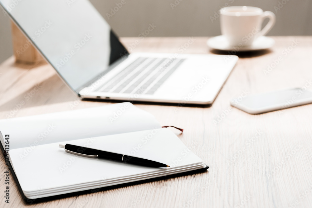 selective focus of notebook with pen near gadgets on table selective focus of notebook with pen near gadgets on table