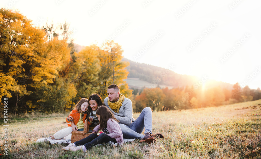 A young family with two small children having picnic in autumn nature at sunset. - obrazy, fototapety, plakaty 