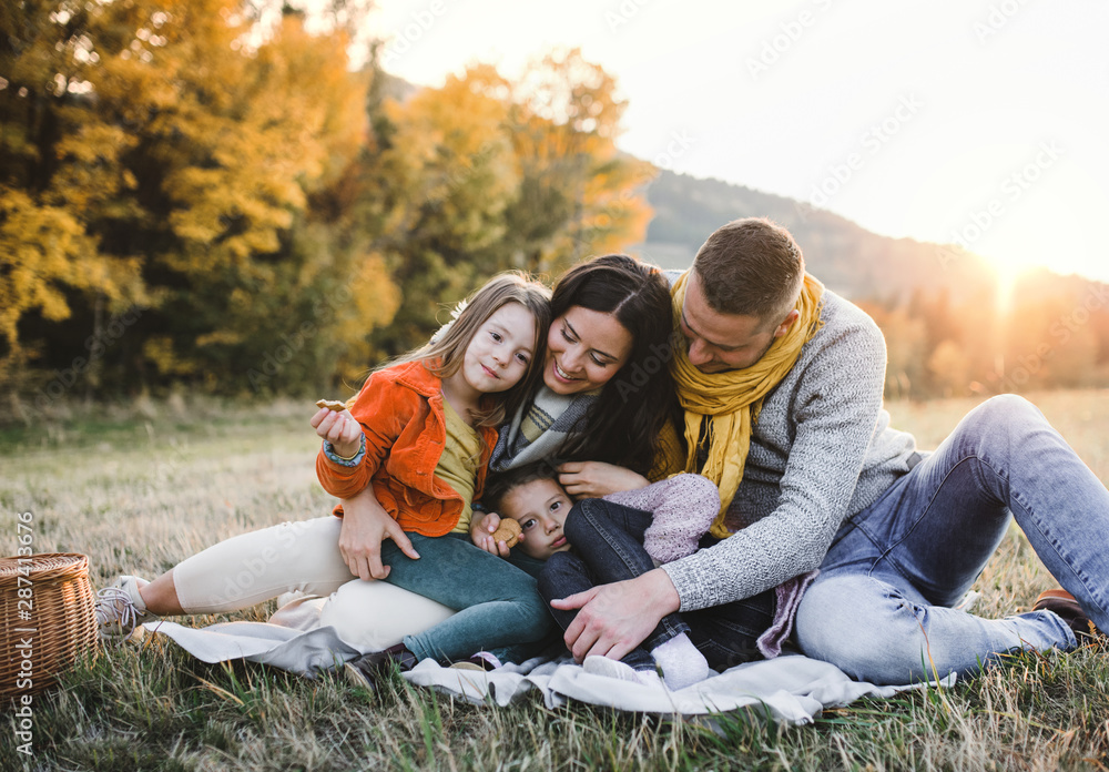 A portrait of young family with two small children in autumn nature at sunset.