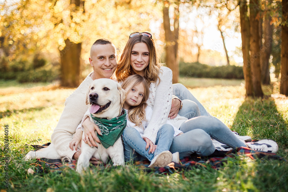 Happy beautiful family with dog labrador is having fun  are sitting on green grass in park.