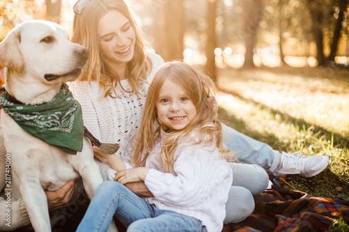 Happy beautiful family with dog labrador is having fun  are sitting on green grass in park.