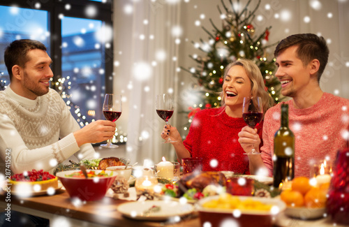 holidays and celebration concept - happy friends having christmas dinner at home and drinking red wine over snow
