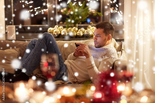 christmas, technology and holidays concept - man with smartphone texting message at home over snow