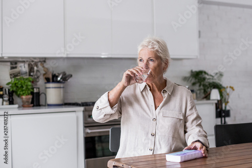 Mature adult woman taking medicine at home in the kitchen