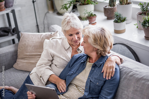 Mature lesbian couple looking at digital tablet together on sofa photo