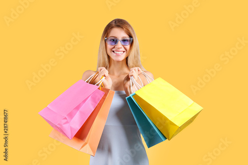 Black friday season sale concept. Attractive young woman with long blonde hair, wearing sexy tight dress, holding many different blank shopping bags, yellow isolated background. Copy space, close up