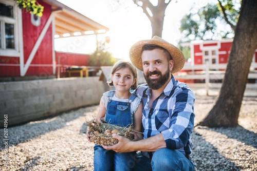 A father with small daughter outdoors on family farm, holding eggs. © Halfpoint