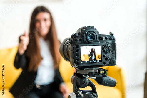 selective focus of digital camera with happy video blogger showing thumb up on screen