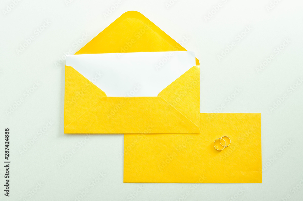 Gold wedding rings on the yellow letter invitation on the white background. Gold wedding rings on the yellow letter invitation on the white background.